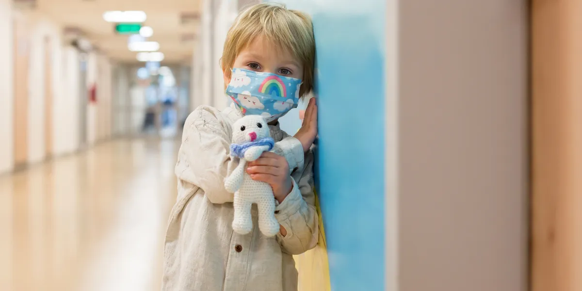 6802b7b47a020_rs=w_1200,h_600,cg_true A child wearing a mask holding a stuffed animal.